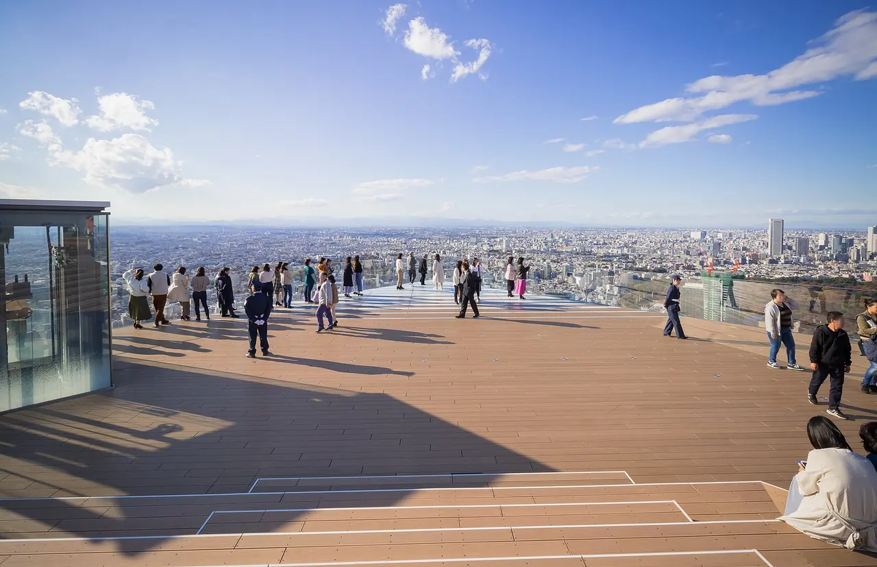 The Sky Edge corner of the SHIBUYA SKY roof on a clear afternoon, with visitors at the glass and Tokyo stretching to the horizon