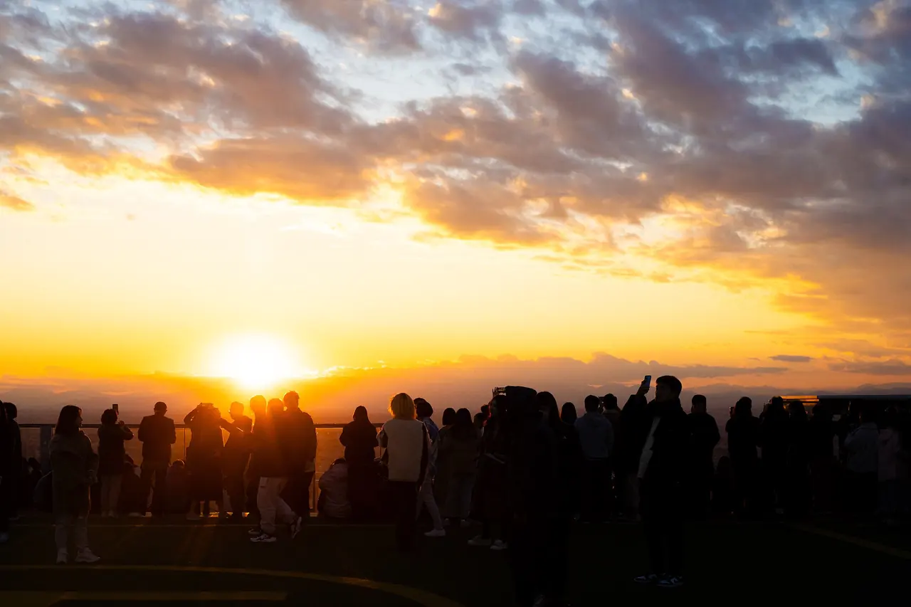 Visitors silhouetted against the setting sun on the SHIBUYA SKY roof, with orange cloud over the city