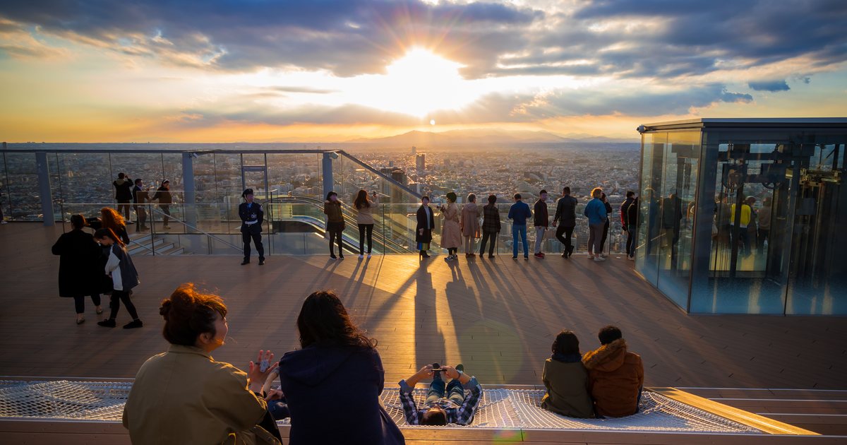 Visitors on the SHIBUYA SKY roof at sunset, with the glass edge and the Tokyo skyline behind